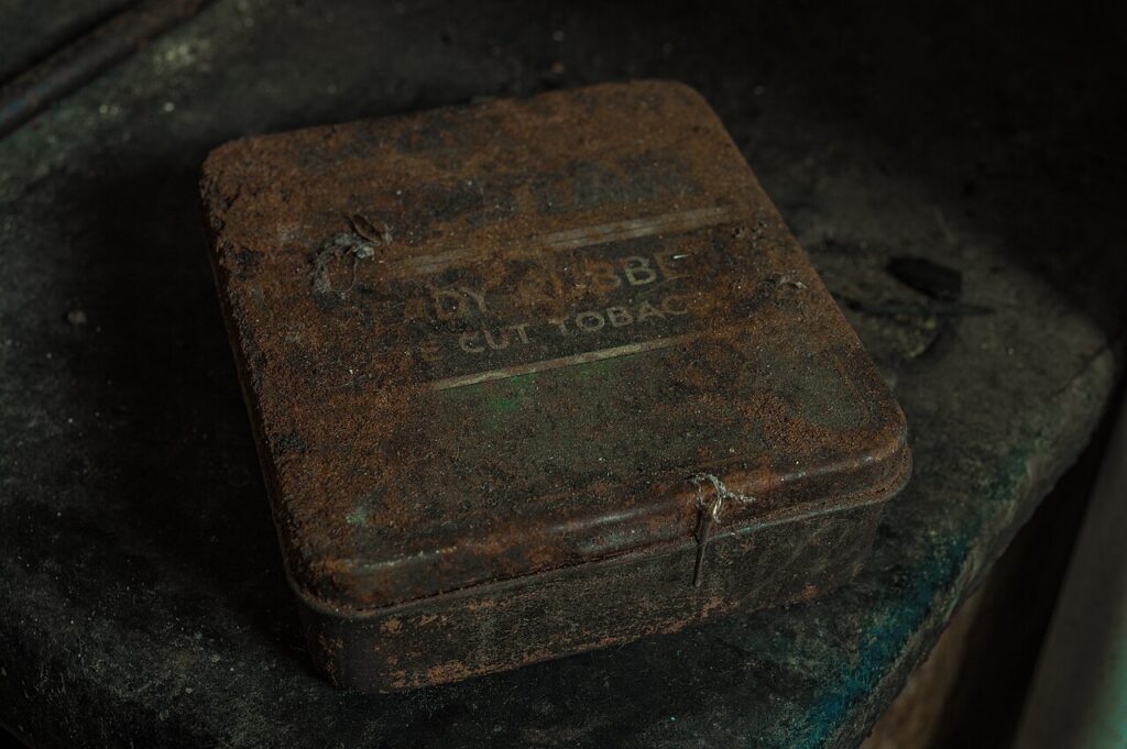 A flat rectangular tobacco tin with heavy rust and faded lettering on its closed lid.
