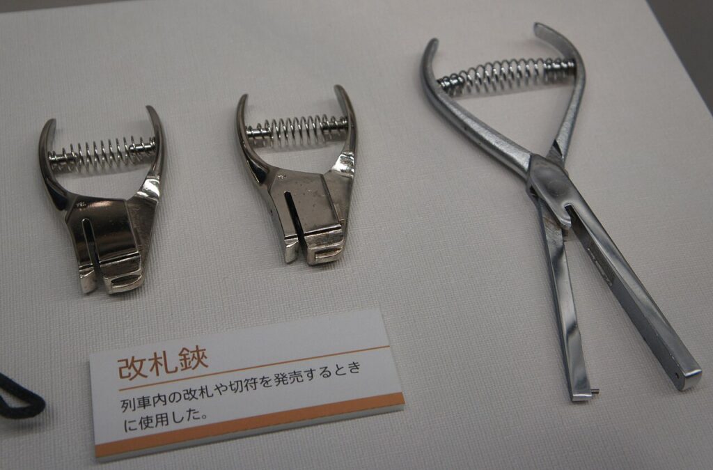 Three metal ticket punches with exposed springs displayed beside a Japanese museum label.